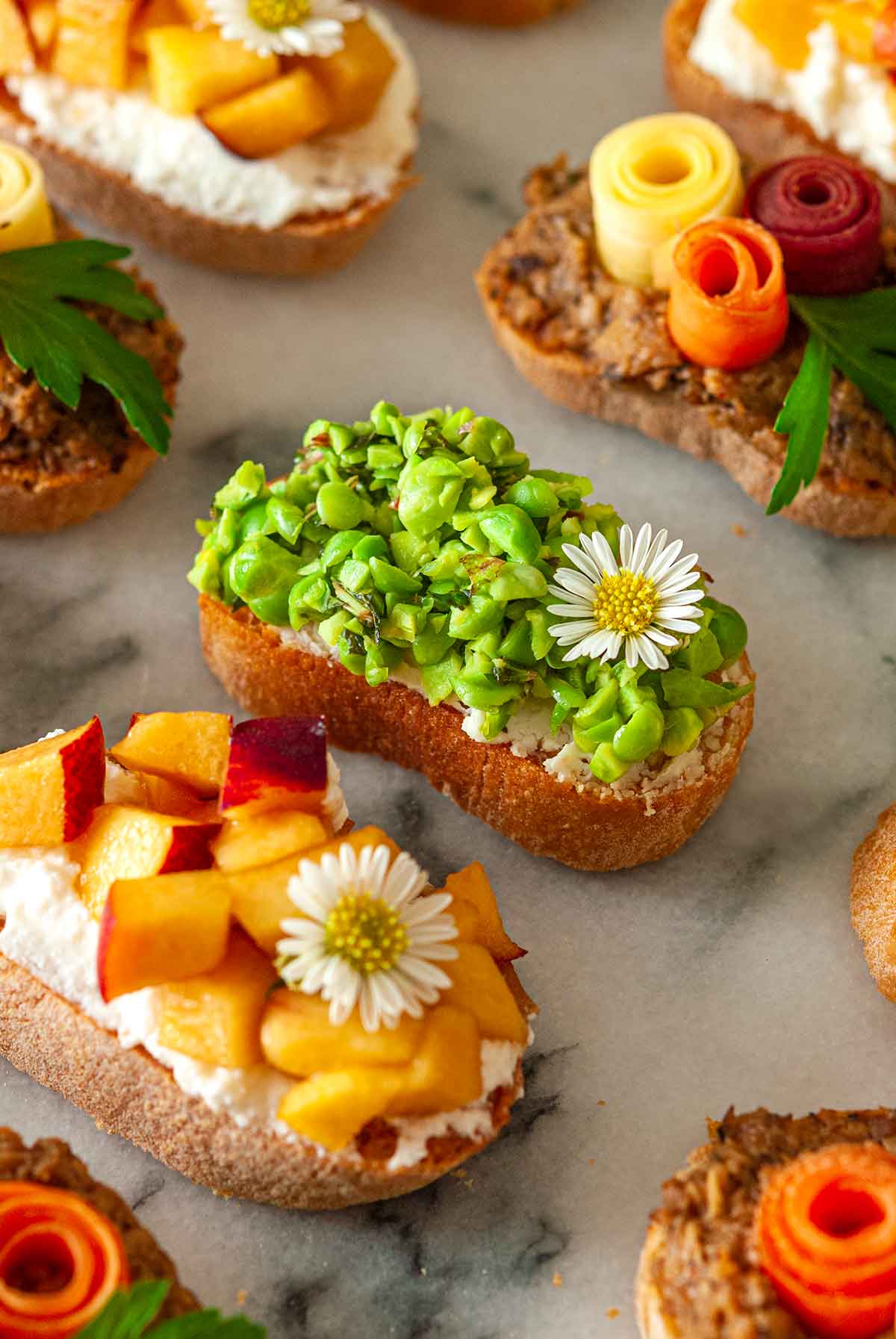 8 brightly colored crostini on a marble slate, with a pea crostini in the center..