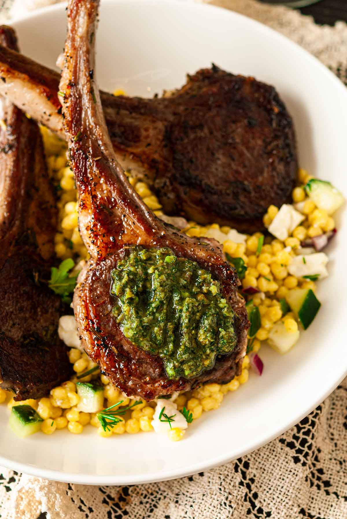 A lamb chop with mint pesto in a bowl with 2 others, on top of pearl couscous.