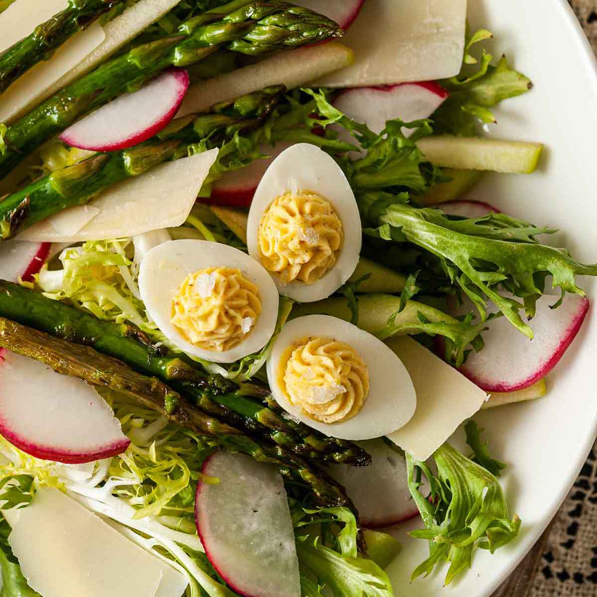 A salad with 3 small deviled eggs in a white bowl.