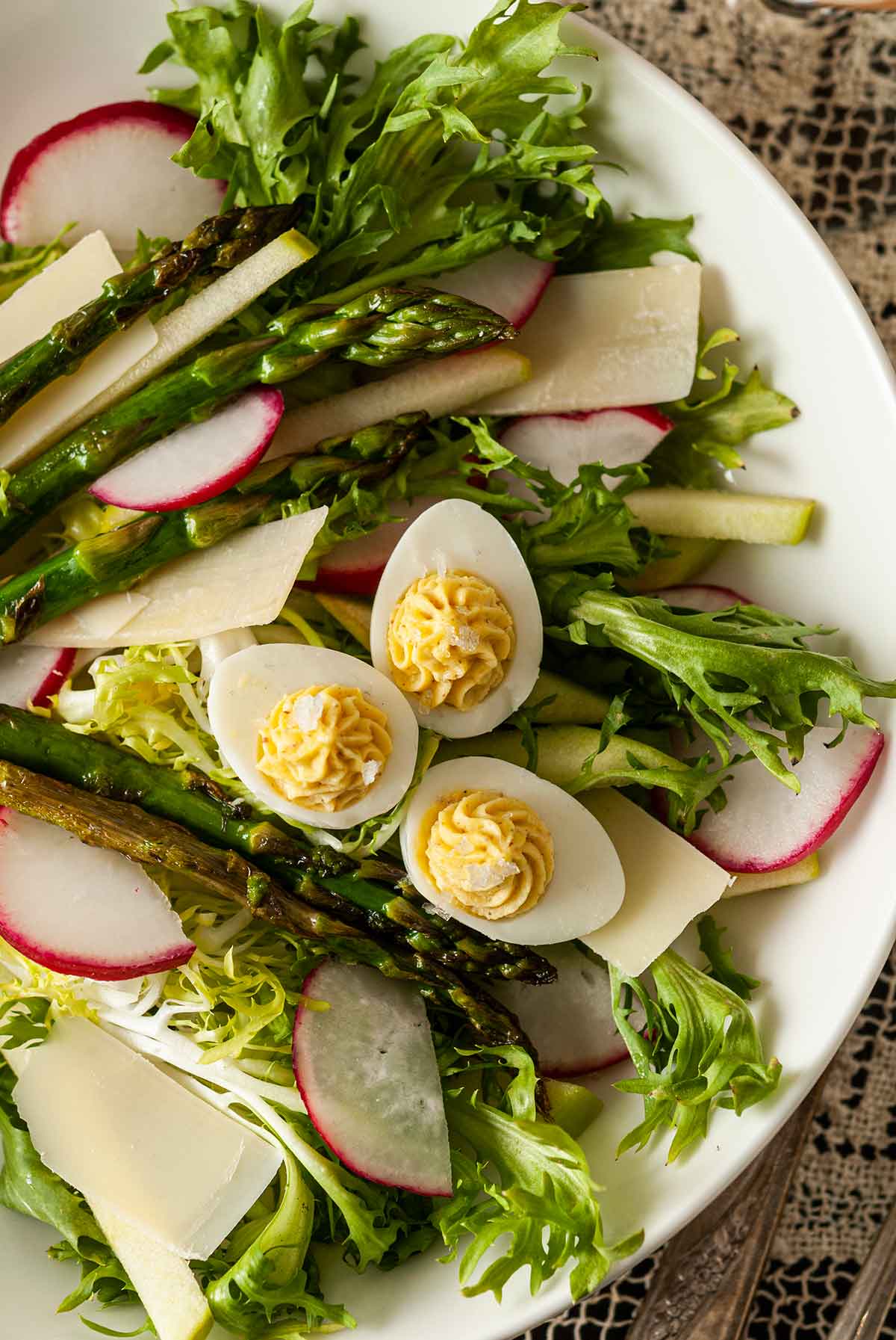 A salad with 3 small deviled eggs in a white bowl.