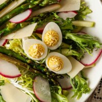 A salad with 3 small deviled eggs in a white bowl.