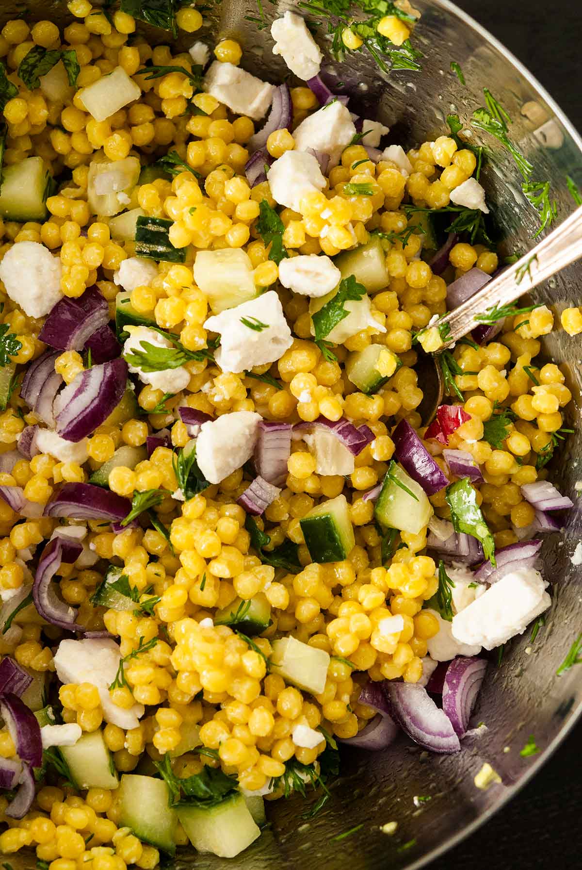 A metal bowl of turmeric couscous mixed with chopped vegetables.