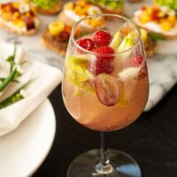 A glass of sake sangria, full of fruit, on a table beside appetizers.