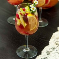 A glass of sake sangria, full of fruit, beside a lace table cloth.