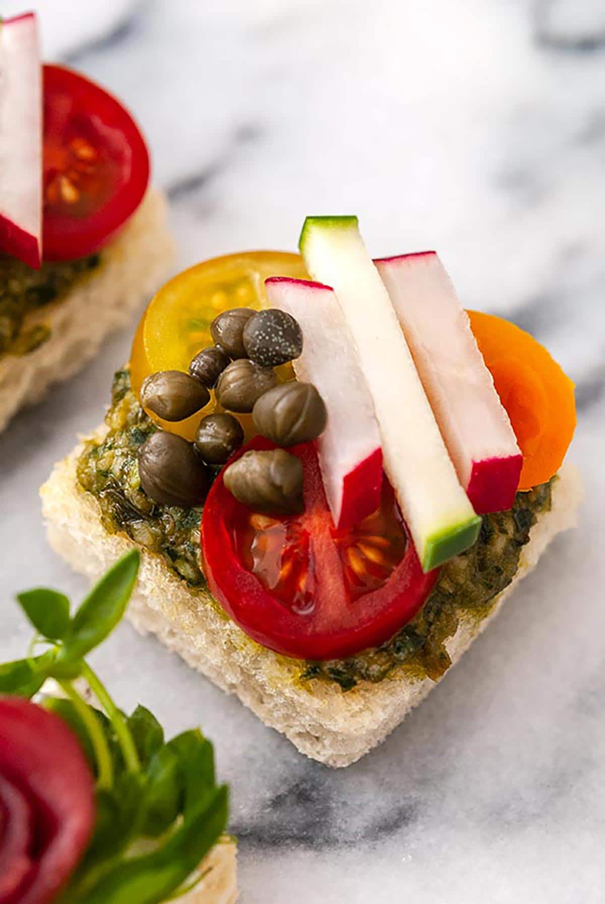 A canapé with tiny cut vegetables and capers on a marble tray.