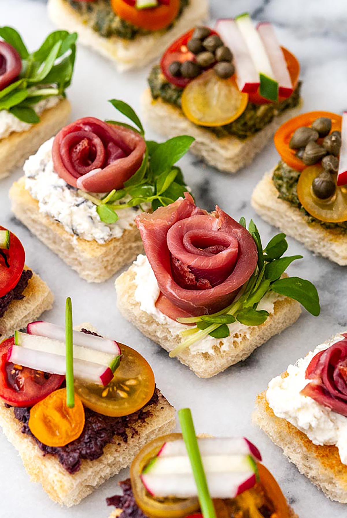 A marble appetizer tray of 9 canapés in 3 different styles.