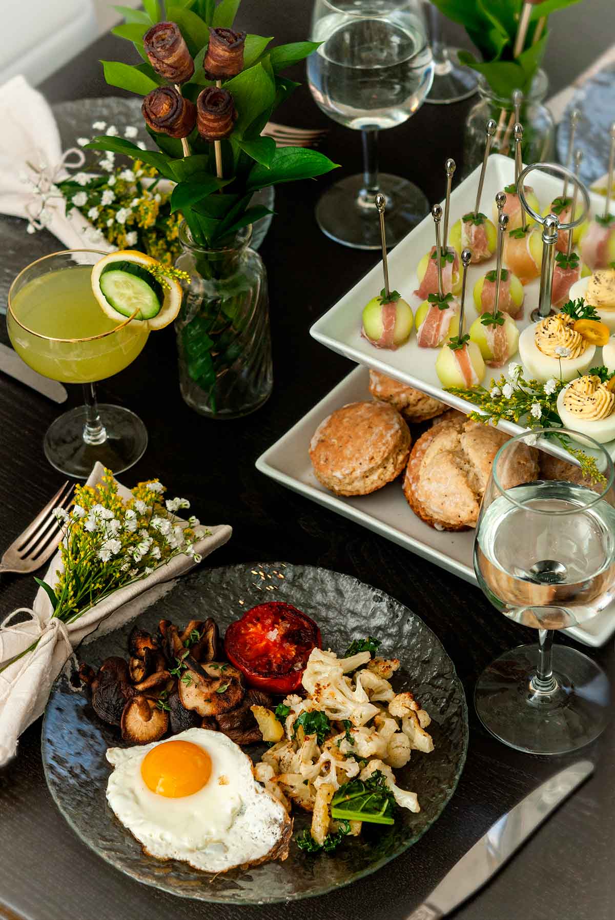 An ornately decorated table with breakfast foods, glasses of water and cocktails.