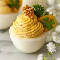 3 deviled eggs, garnished with tomato, clover, parsley and a dollop of mustard caviar on marble.