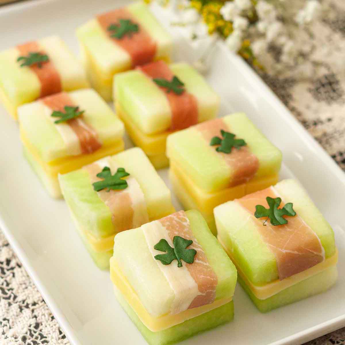 8 St. Patrick's Day melon appetizers with clovers on top, on a white plate, on a lace table cloth..
