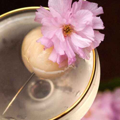 A lychee and cherry blossom garnish on the edge of a cocktail.