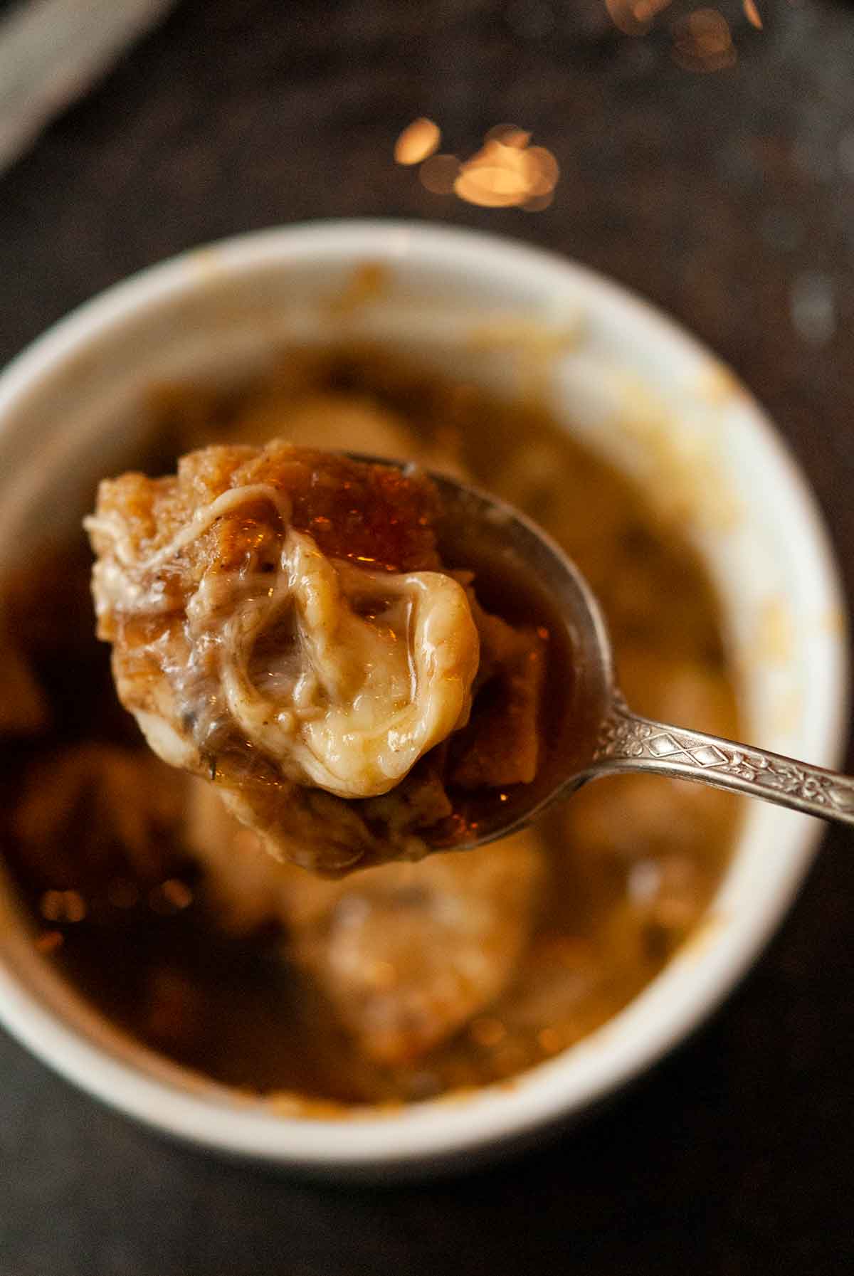 A spoon holding melted cheese and soup over a soup bowl.