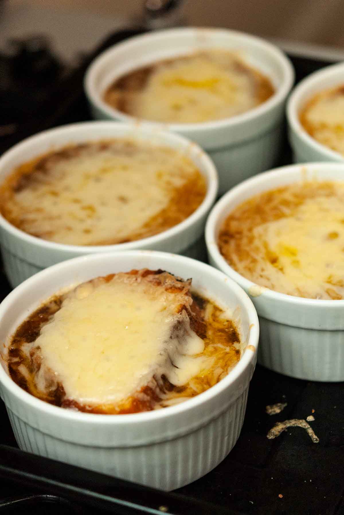 5 bowls of french onion soup with melted cheese.