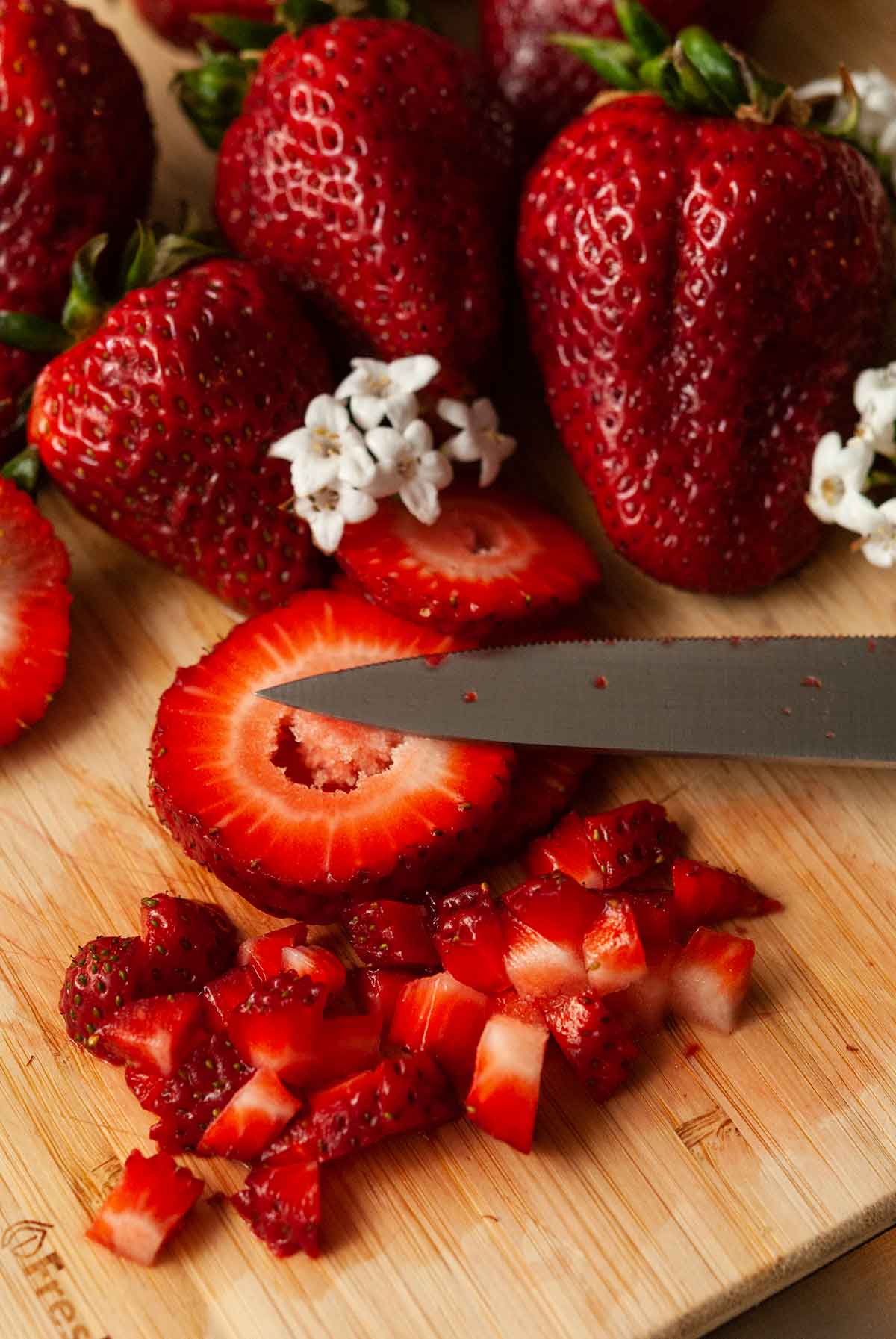 Sliced strawberries on a butting board with other whole strawberries and flowers.