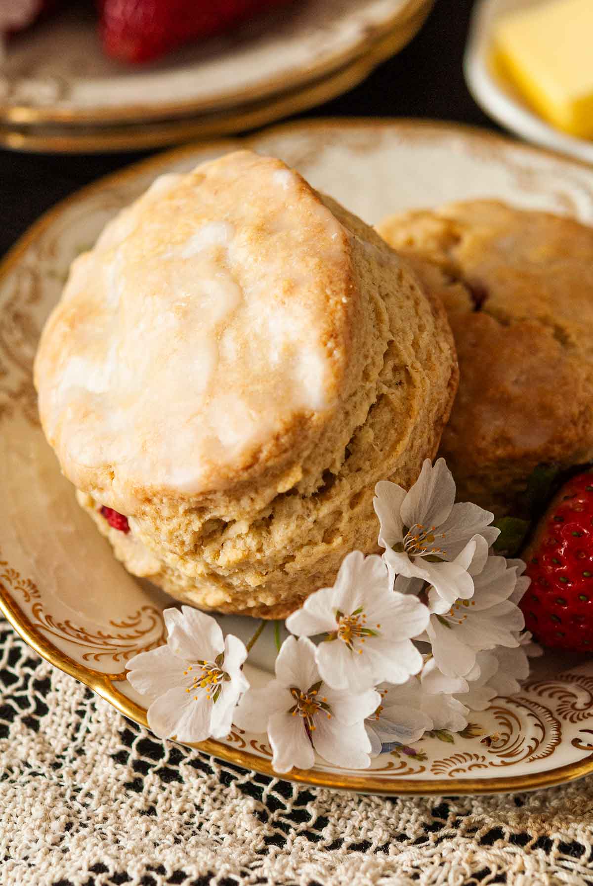 The glaze on one of 2 scones on a plate with flowers.