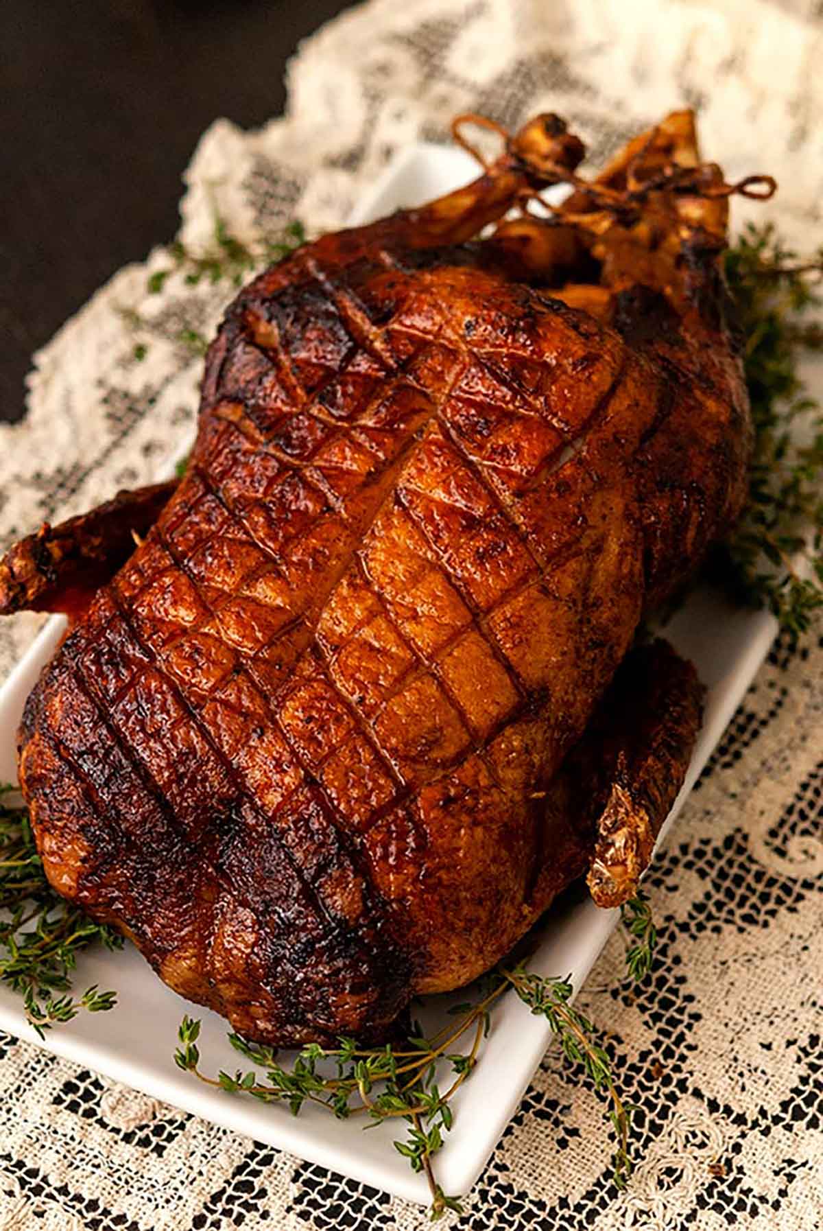 A roasted duck on lace table cloth, garnished with thyme.