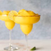 2 frozen mango margaritas on a table beside a sliced lime.