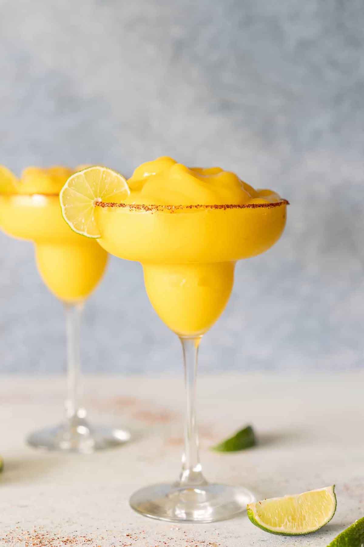 2 frozen mango margaritas on a table beside a sliced lime.