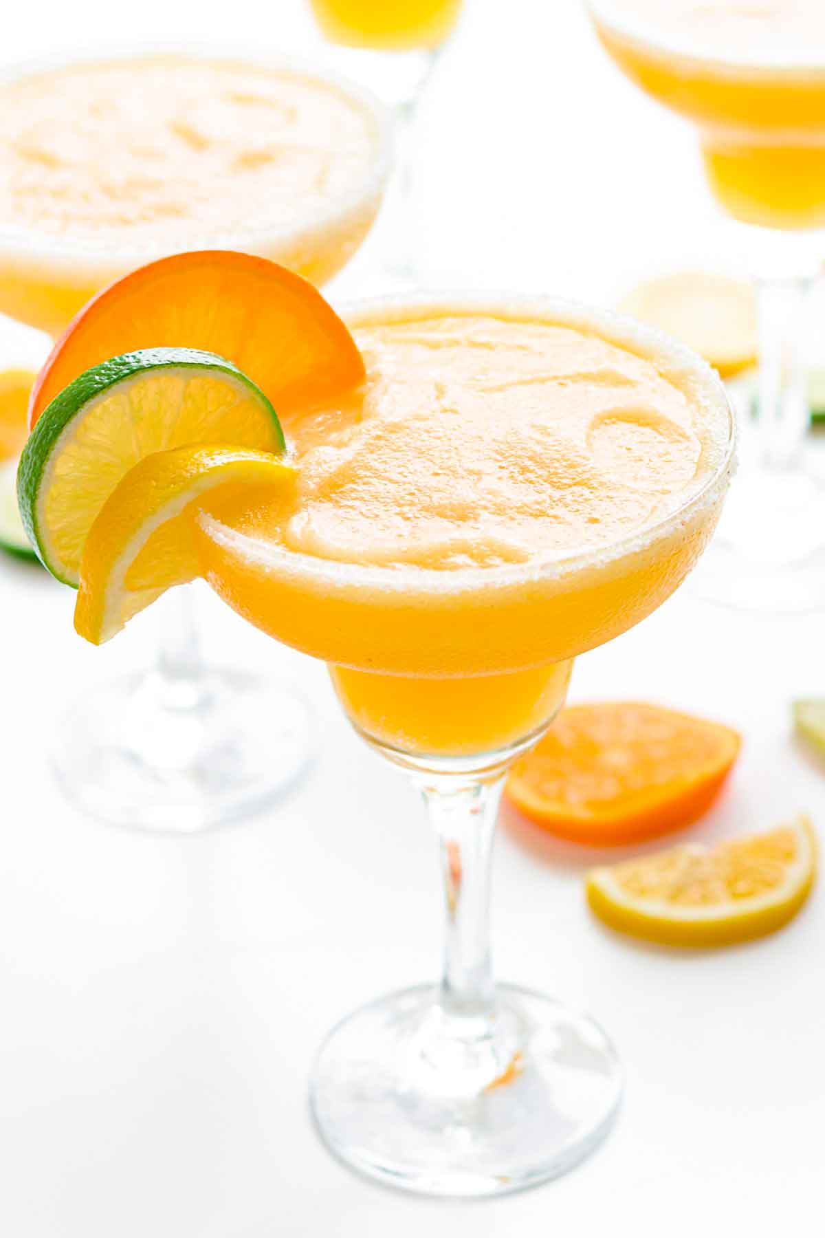 A frozen citrus margarita, garnished with citrus slices, surrounded by other cocktails.