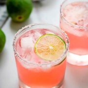 2 hibiscus margaritas on a table, garnished with lime.