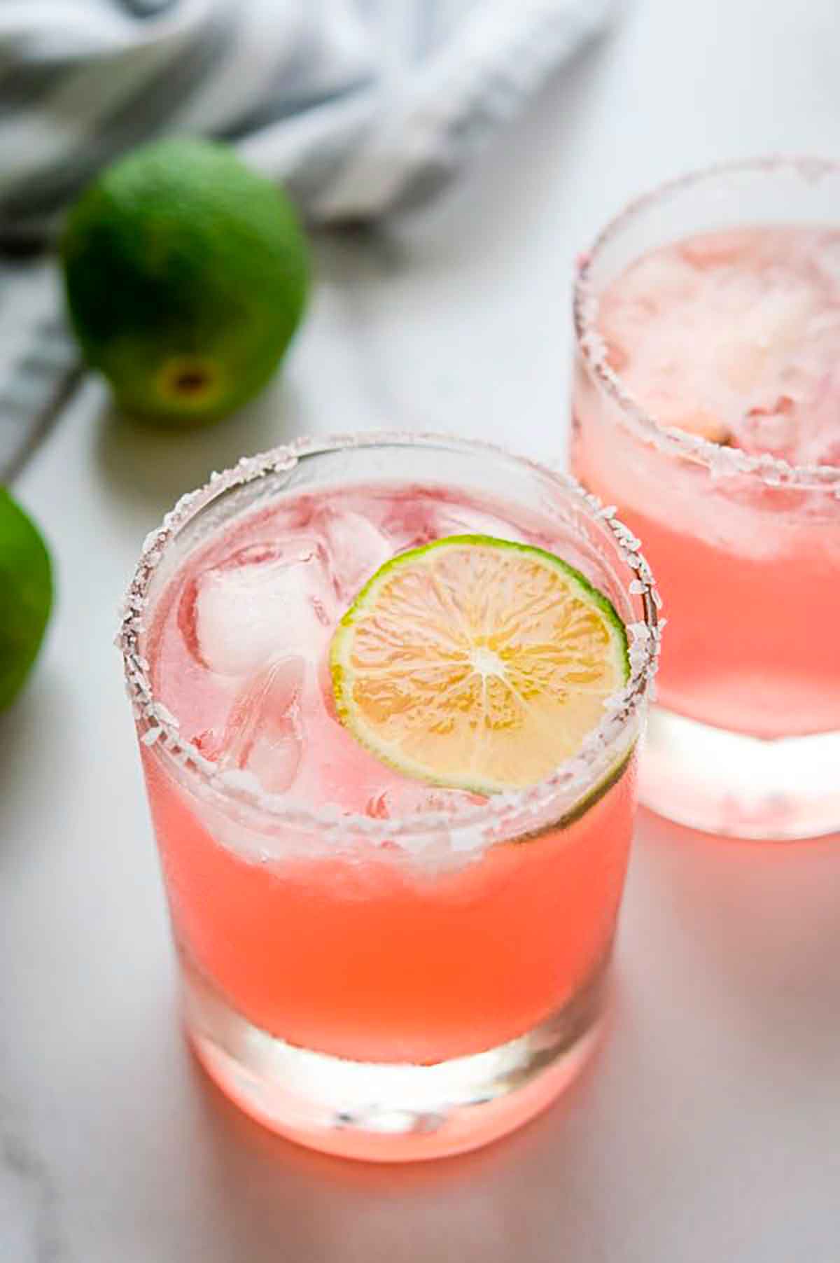 2 hibiscus margaritas on a table, garnished with lime.