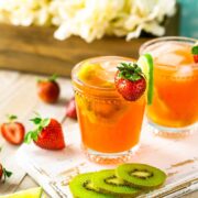 2 strawberry margaritas on a cutting board, beside slices of kiwi, strawberries and lime slices.