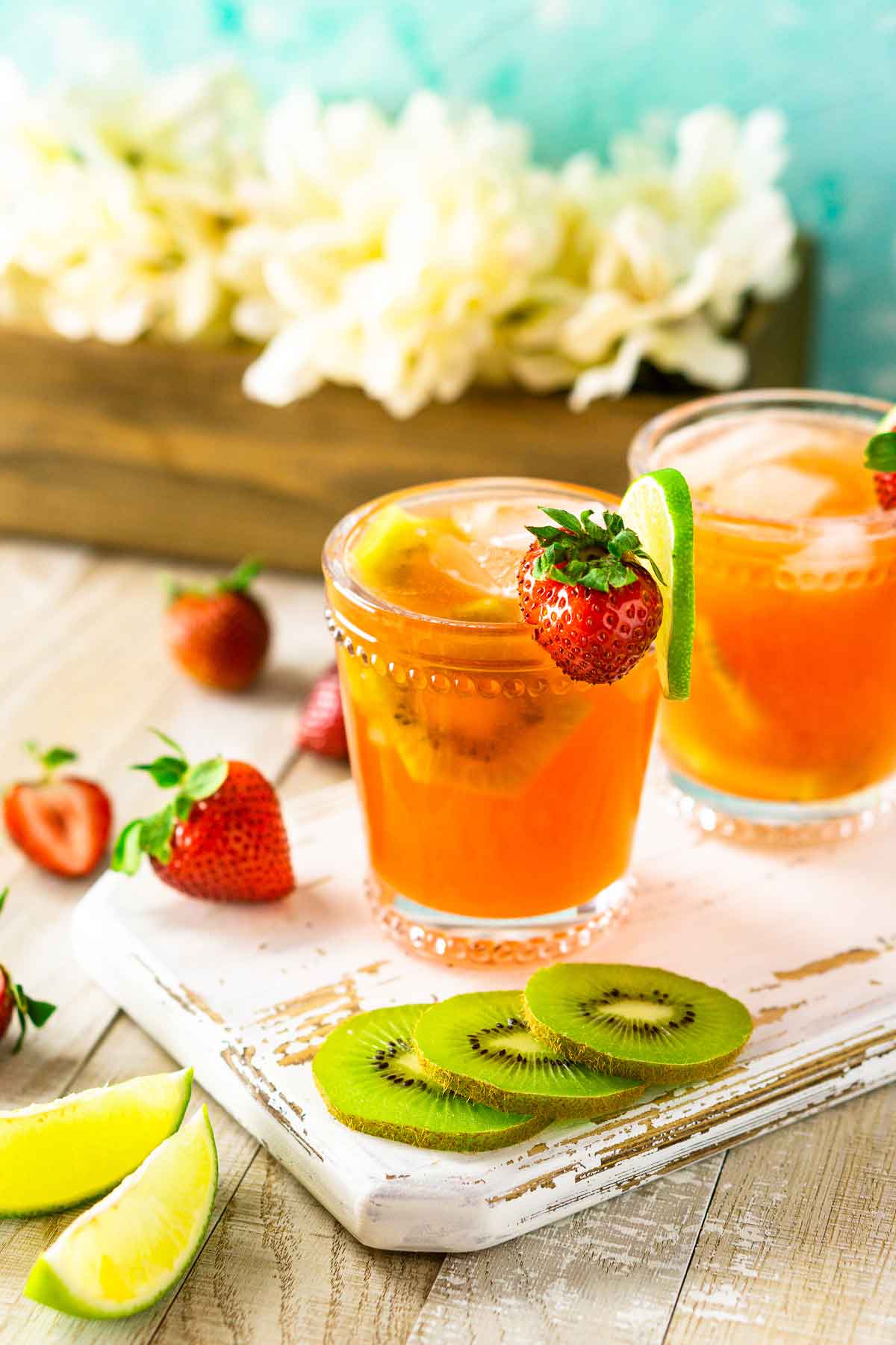 2 strawberry margaritas on a cutting board, beside slices of kiwi, strawberries and lime slices.