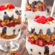 3 parfaits with berries, granola and cream on a table.