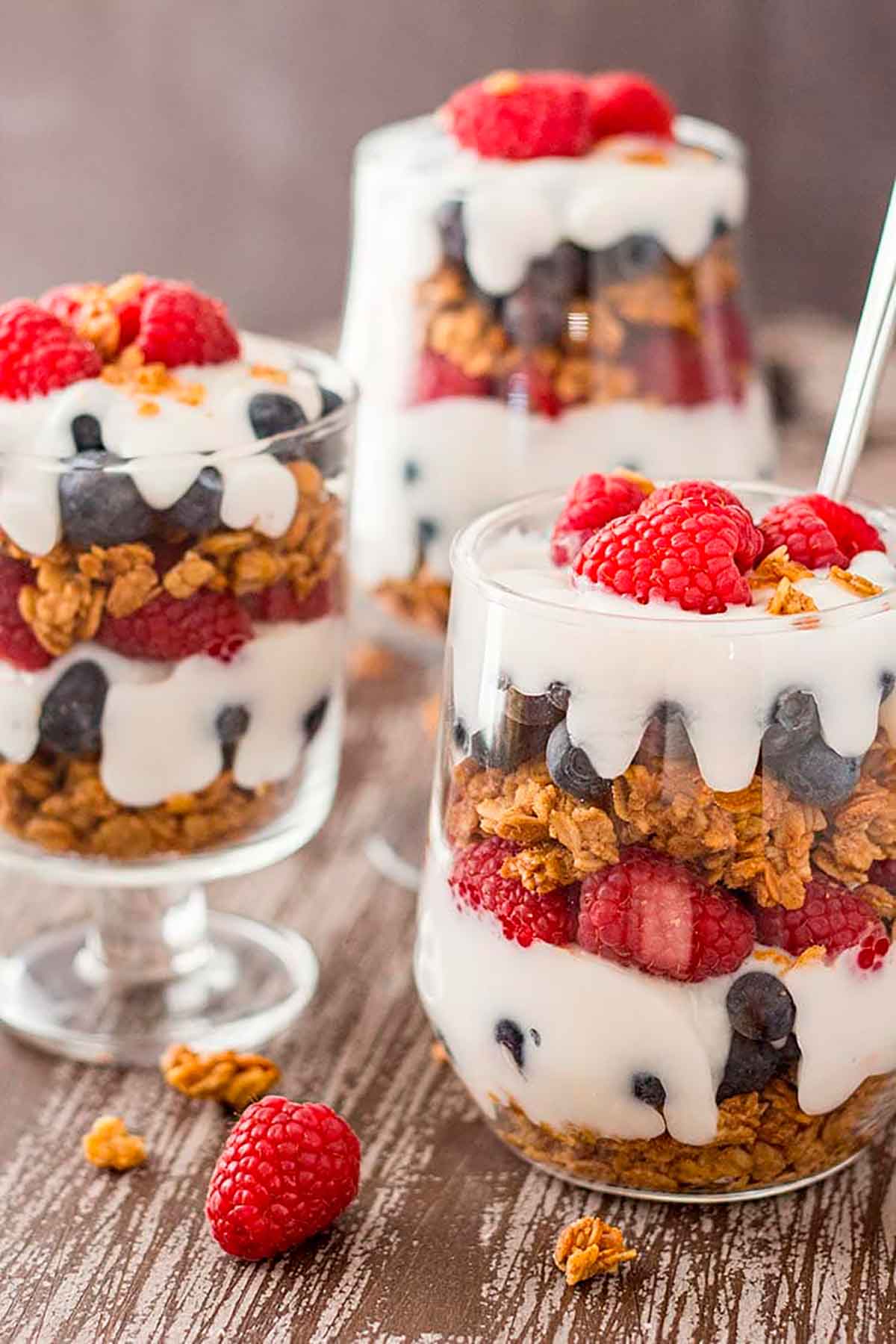 3 parfaits with berries, granola and cream on a table.