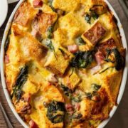 A strata in a baking dish on a table with forks and other servingware.