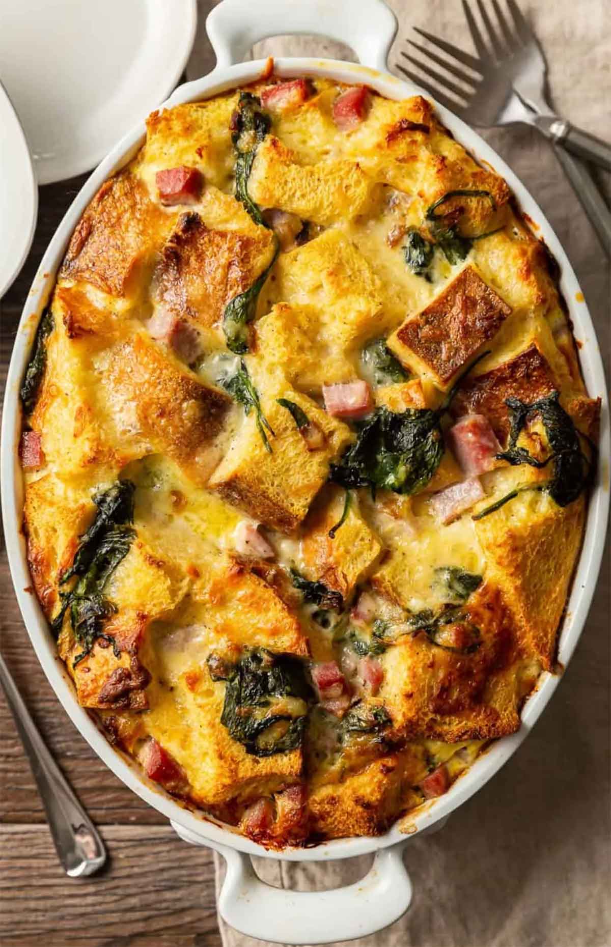 A strata in a baking dish on a table with forks and other servingware.