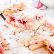 A spatula holding up a strawberry cheesecake danish above a full danish in a baking dish.