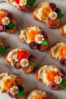 Crostini garnished with daisies, onions and tomatoes on a marble plate