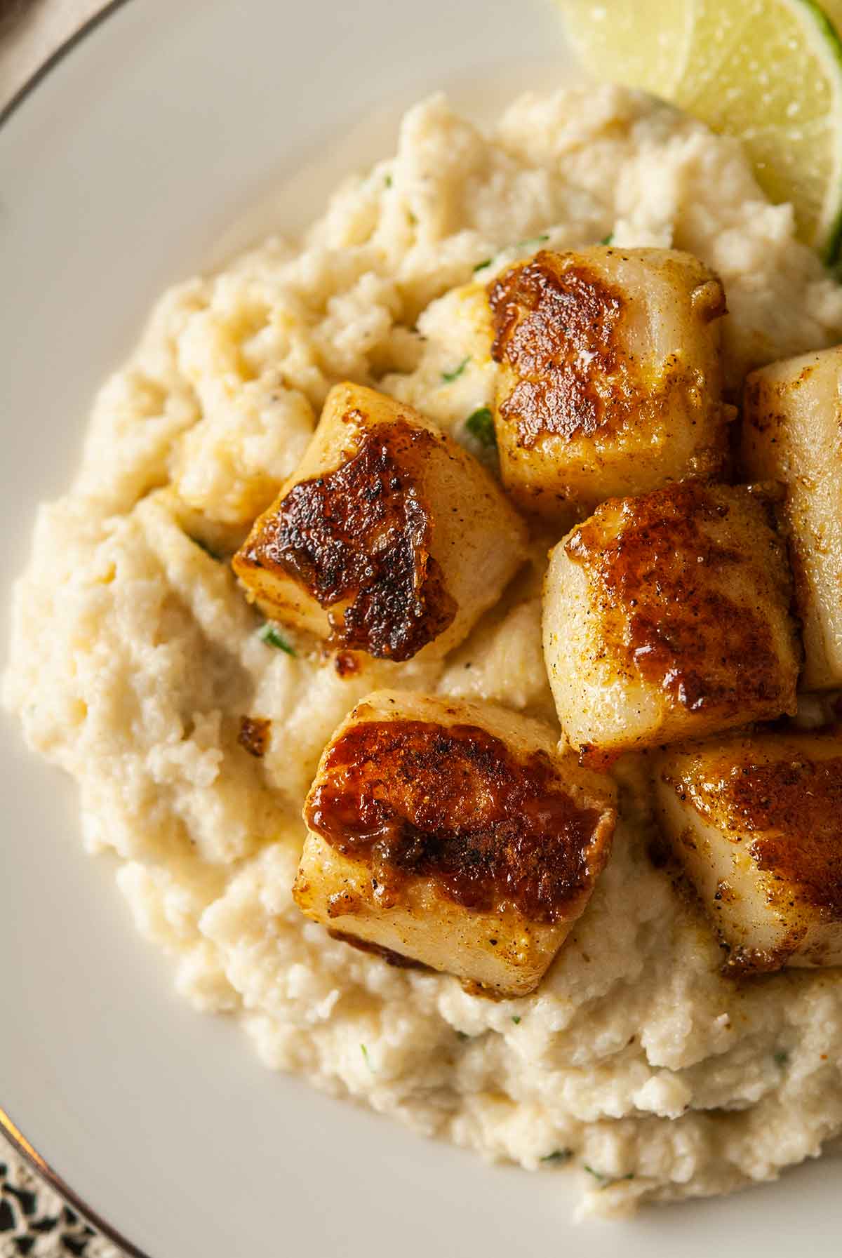 6 curry-seared scallops on a plate with mashed cauliflower.