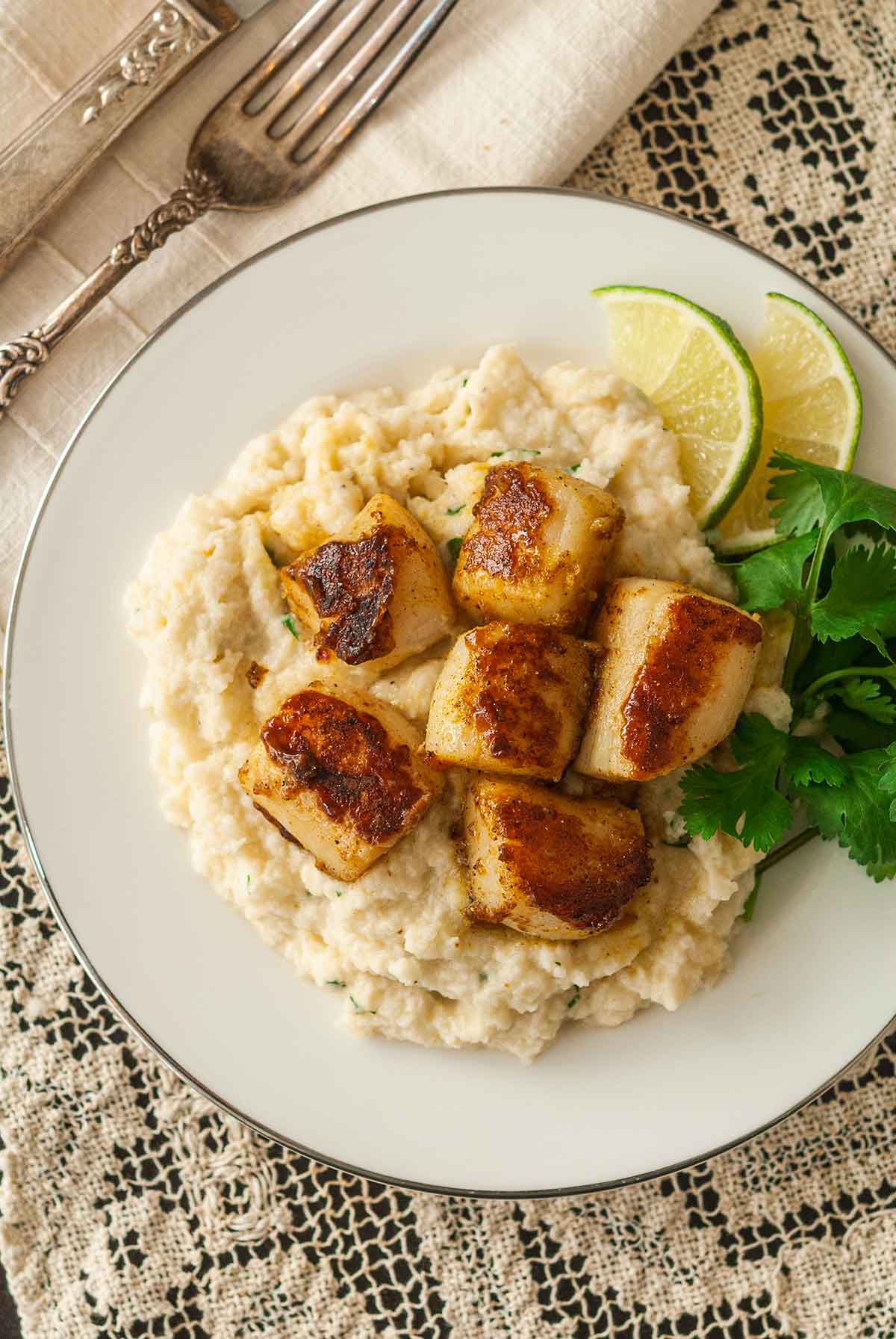 6 curry-seared scallops on a plate with mashed cauliflower, parsley and 2 lime slices.