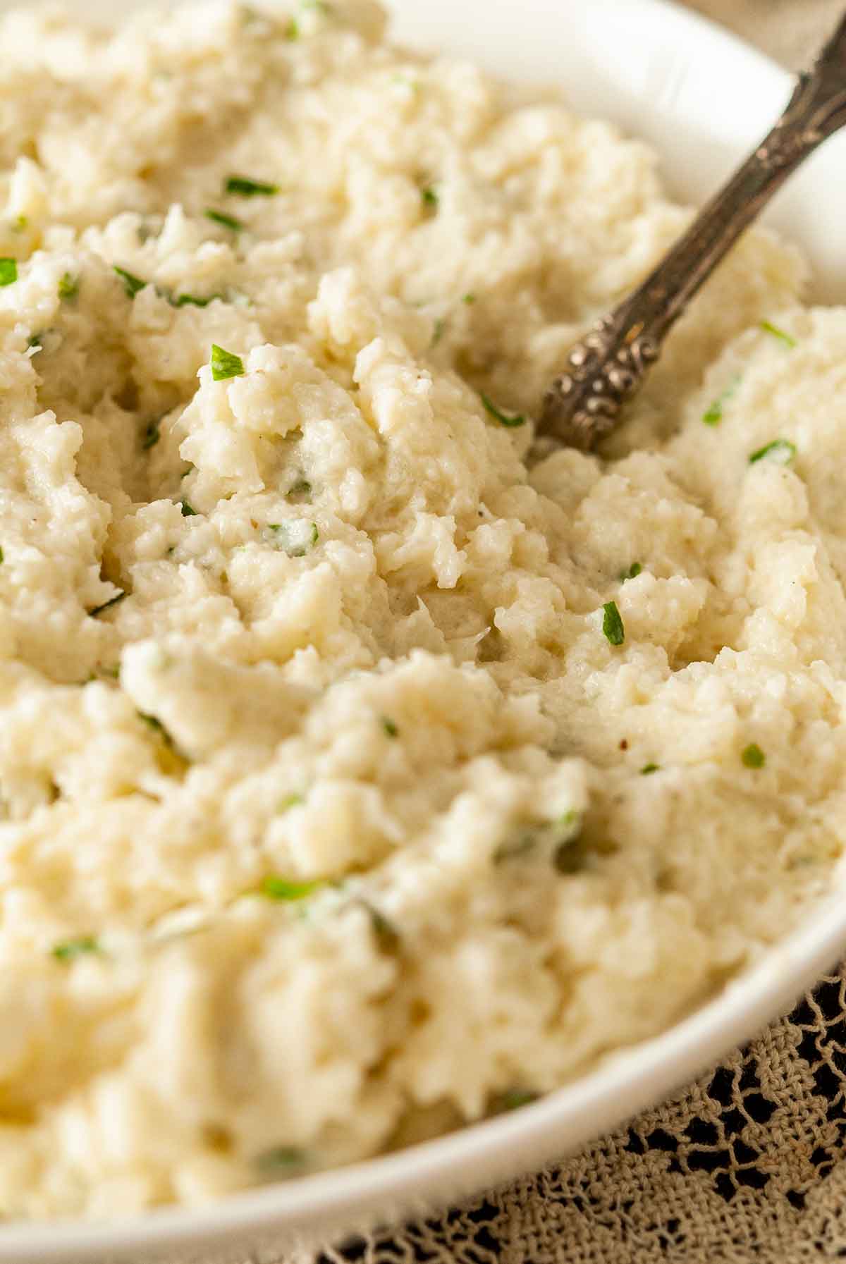 A bowl of garlic-parmesan mashed cauliflower with finely-diced parsley and an antique spoon.