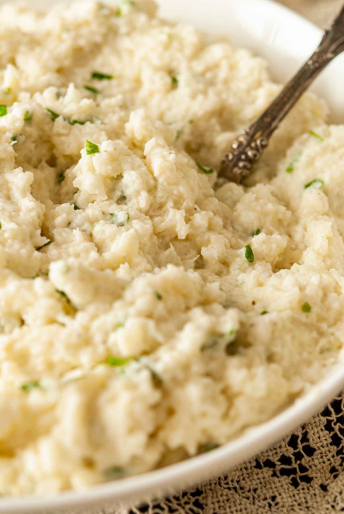 A bowl of garlic-parmesan mashed cauliflower with finely-diced parsley and an antique spoon.