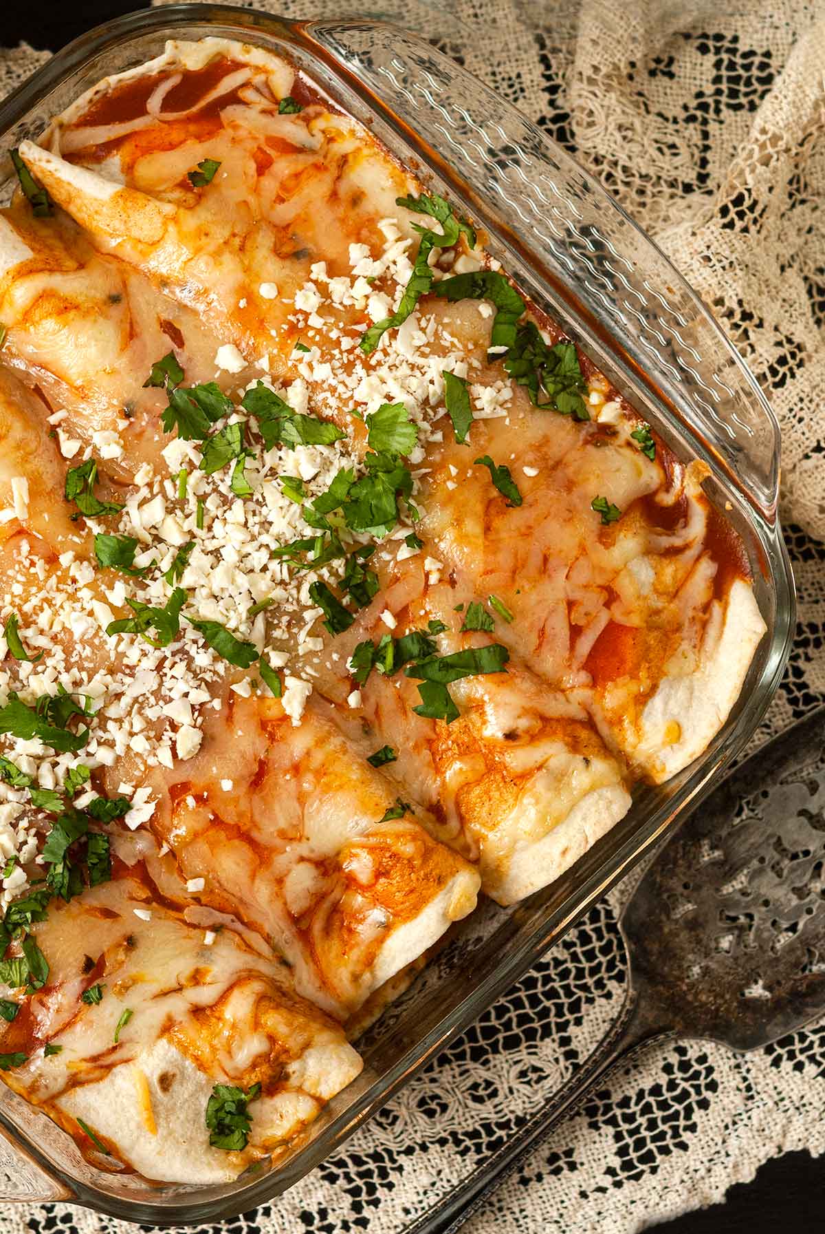 A Pyrex dish with 4 chicken enchiladas on a lace tablecloth.