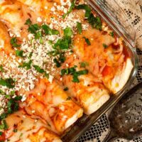 A Pyrex dish with 4 chicken enchiladas on a lace tablecloth.