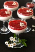 4 glasses of panna cotta with strawberry-rhubarb compote, garnished with flowers, on a table.