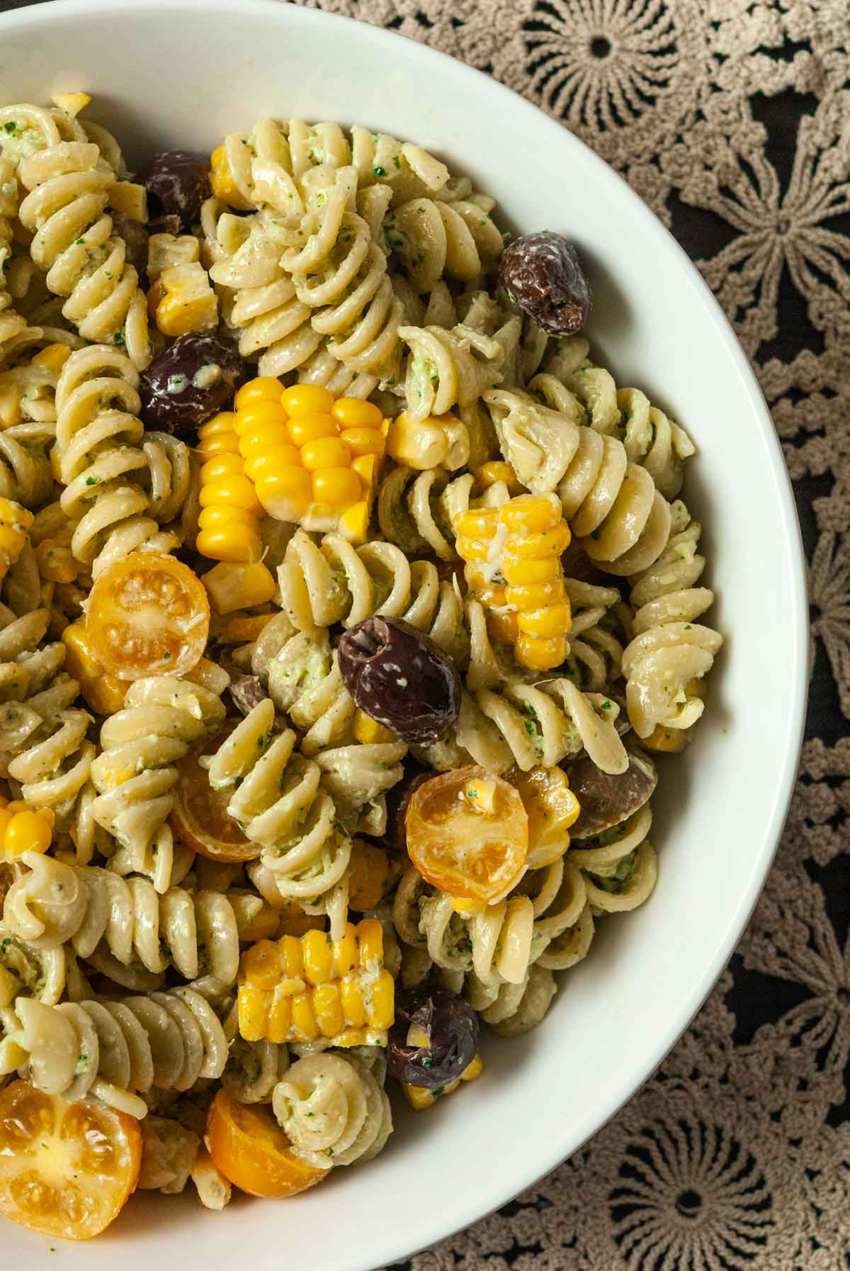 A bowl of pesto pasta salad with corn, olives, cherry tomatoes and mozzarella.