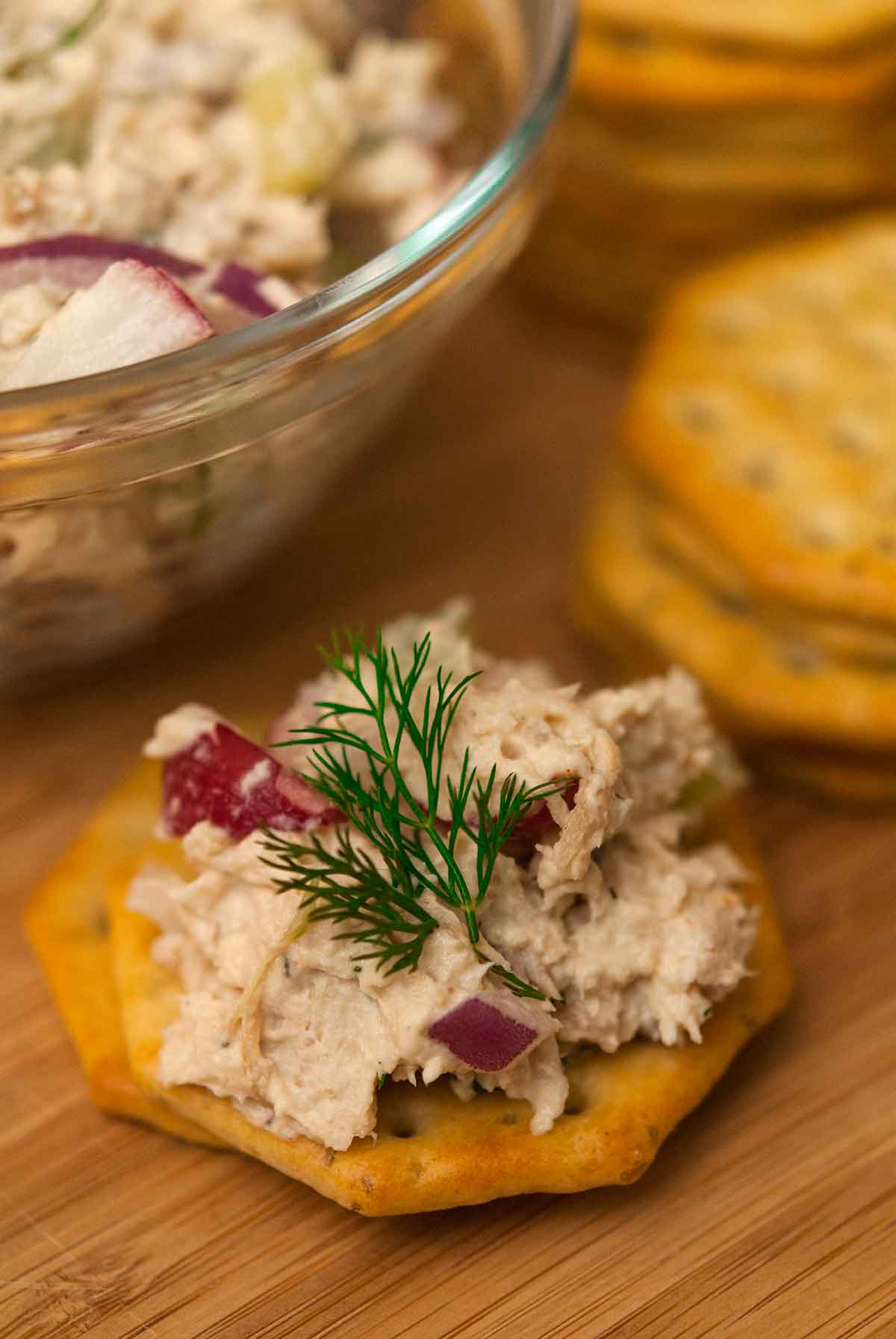 A cracker with chicken salad on a wooden plate.