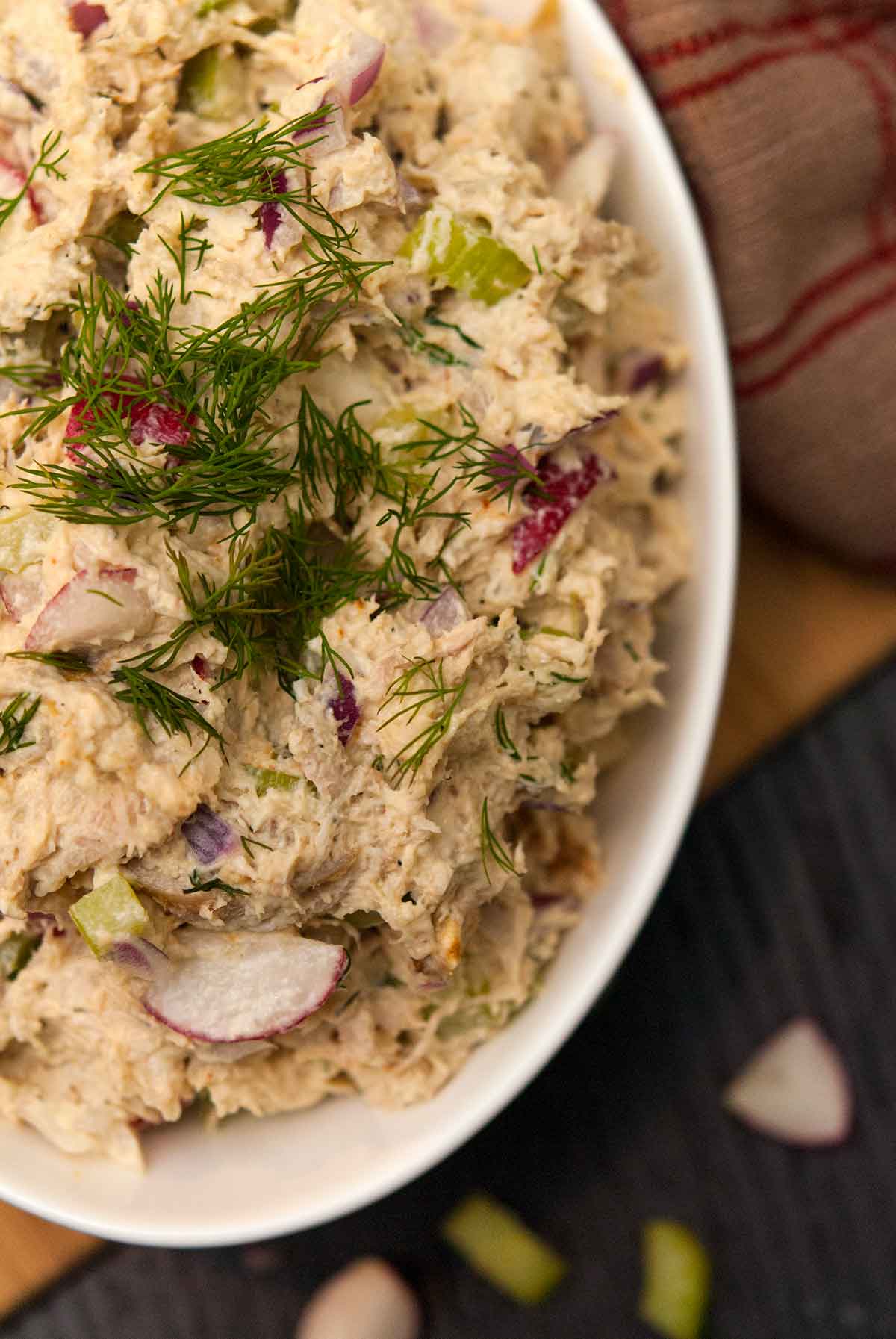 A bowl of chicken salad, topped with dill beside a vintage tea towel.