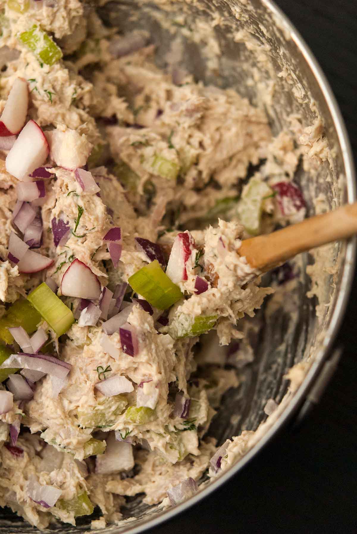 A bowl of chicken salad with vegetables and a mixing spoon.