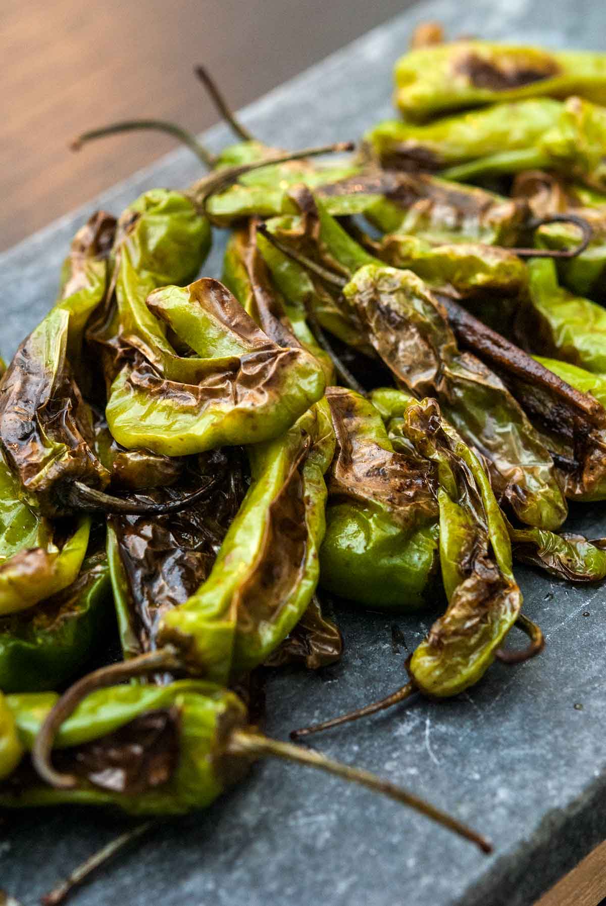 Blistered shishito peppers piled on a slate.