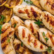 A plate of about a dozen grilled chicken tenders, sprinkled with thyme.