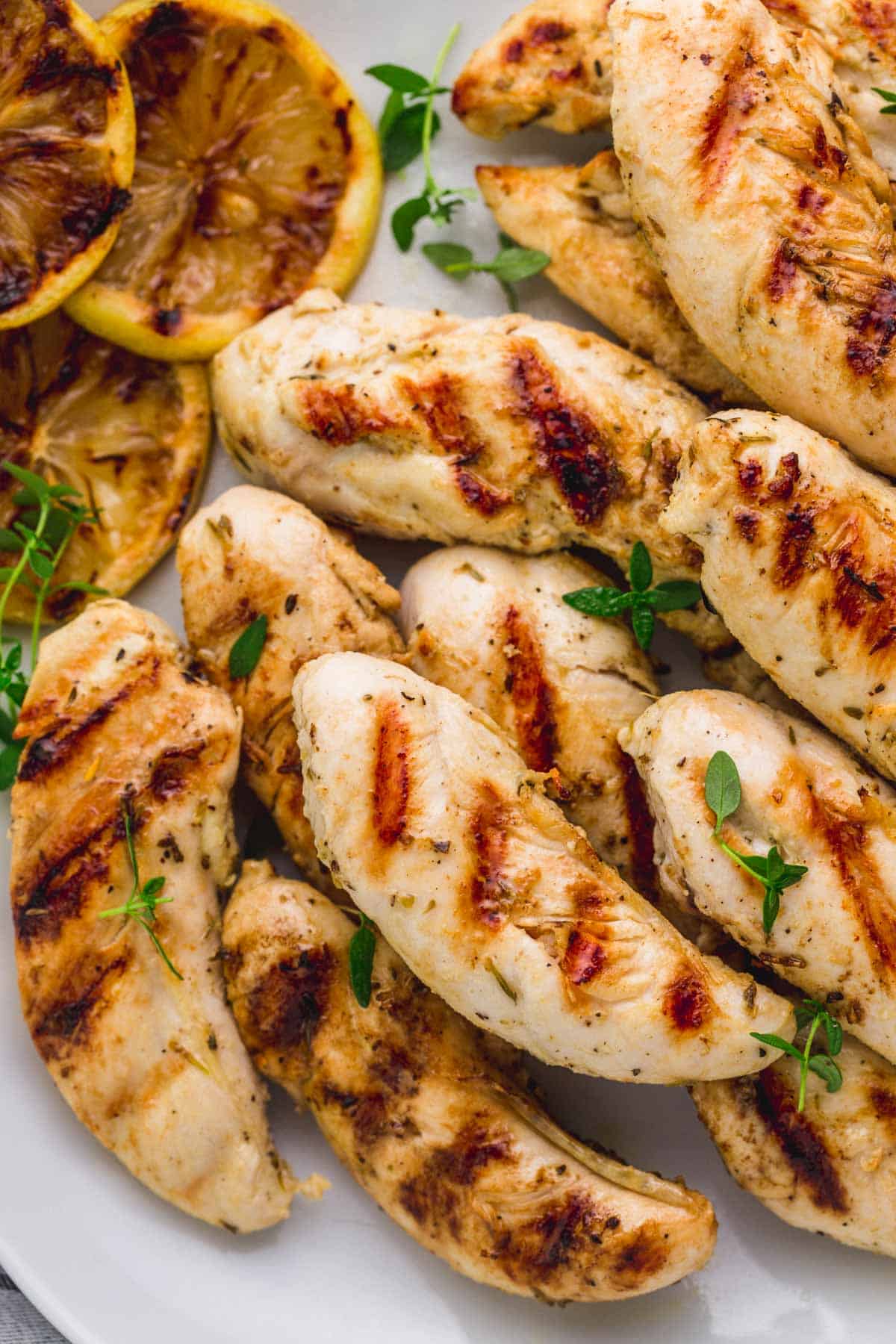 A plate of about a dozen grilled chicken tenders, sprinkled with thyme.