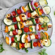 6 skewers on a plate with halumi and vegetables.