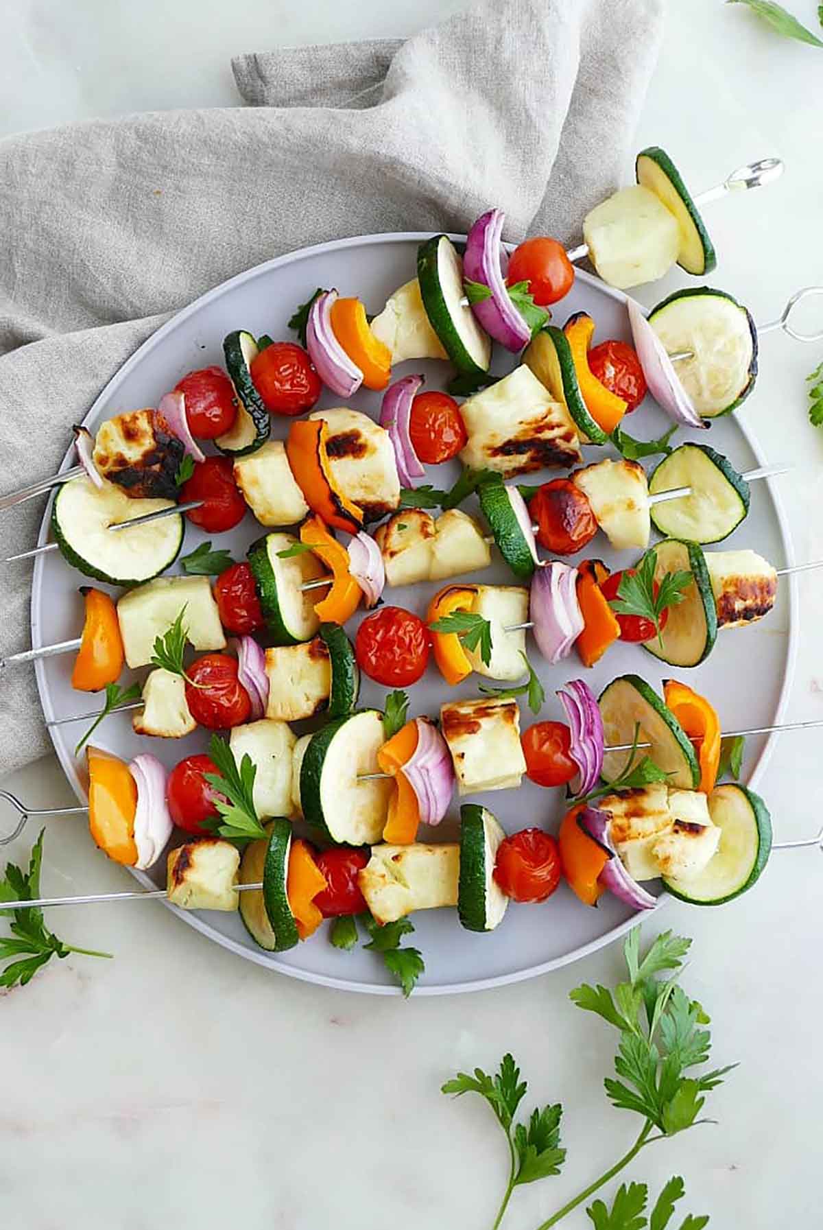 6 skewers on a plate with halumi and vegetables.