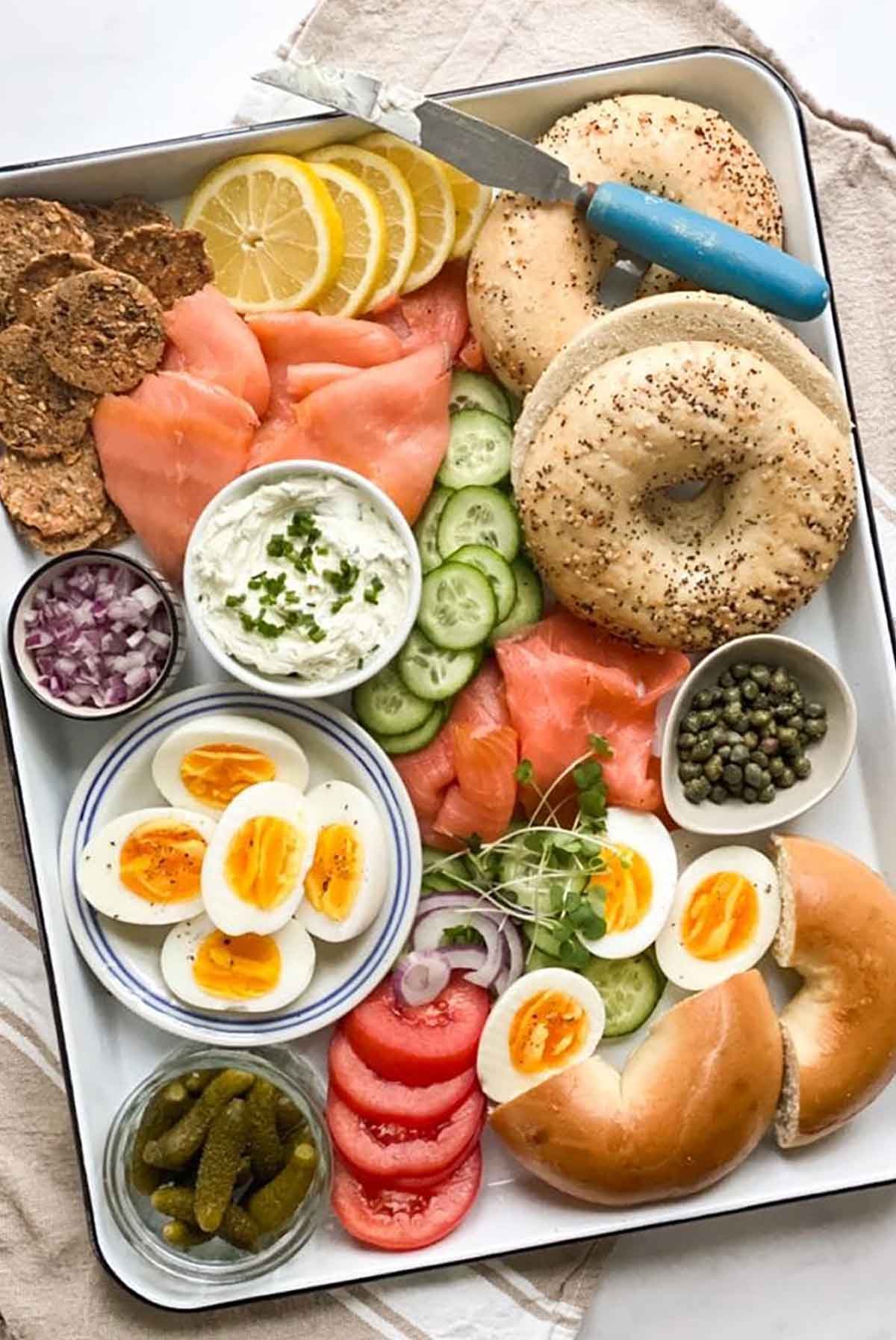 A tray of bagels with scattered, assorted bagel toppings.