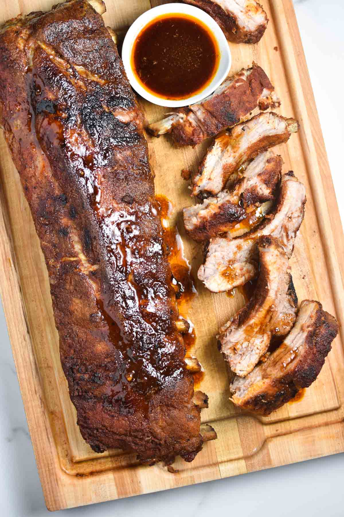 Seasoned, cooked ribs on a cutting board with a sauce.